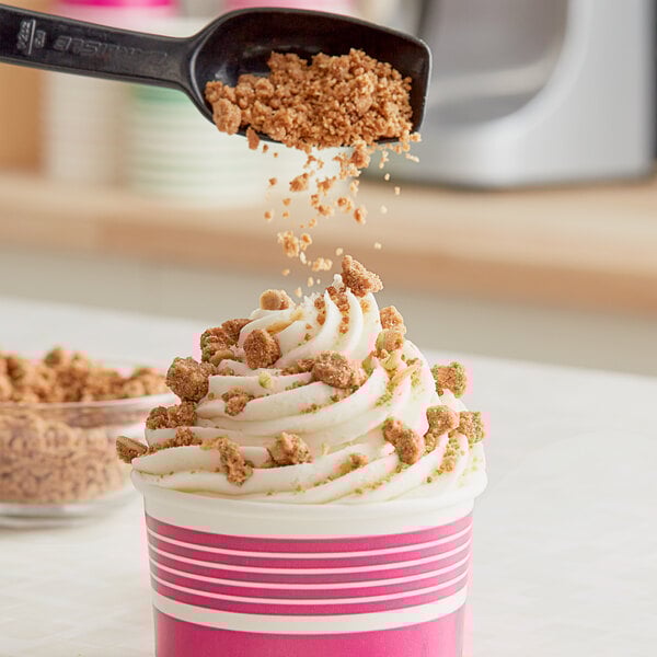 A cup of ice cream with brown crumbles on top from a spoon.