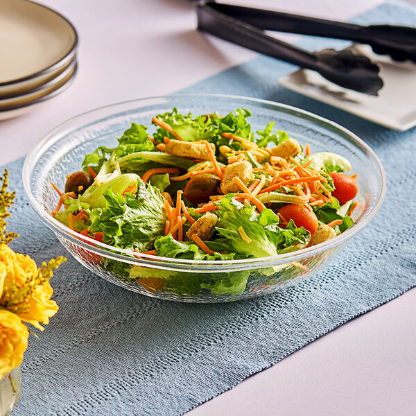 A Carlisle clear pebbled bowl filled with salad on a table.