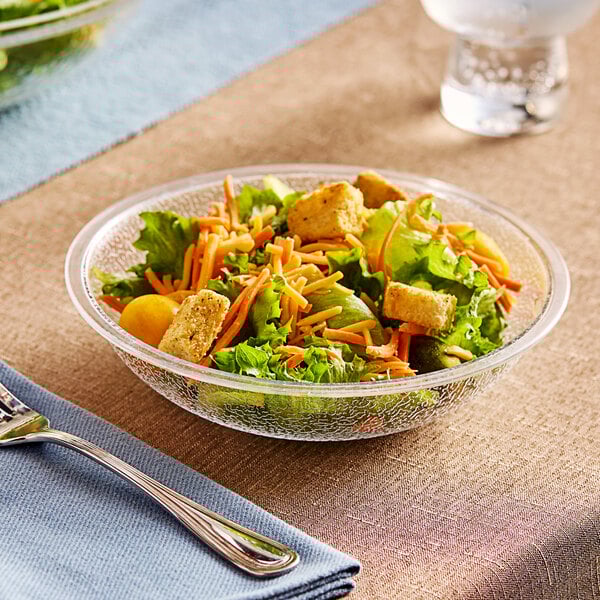 A Carlisle clear pebbled acrylic bowl filled with salad on a table with a fork.
