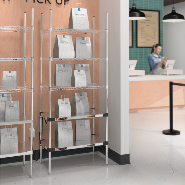 A woman standing in front of a Metro Stainless Steel Takeout Station with heated and chrome shelves full of bags.