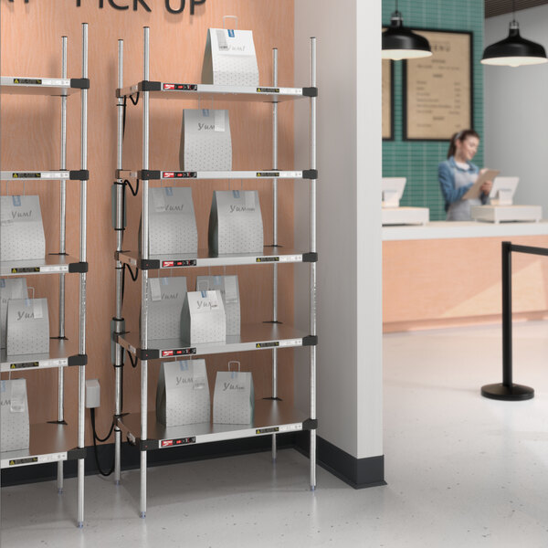 A woman standing in front of a Metro heated stainless steel takeout station shelf with bags on it.