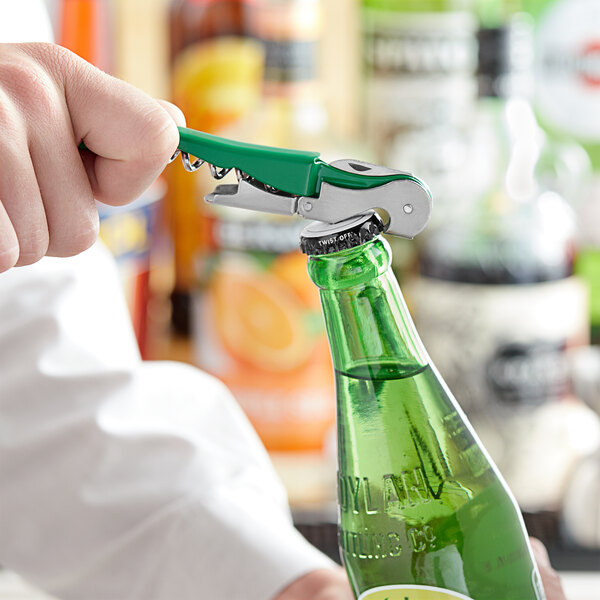 A person using an Acopa Waiter's Corkscrew with a green and silver metal handle to open a green bottle.