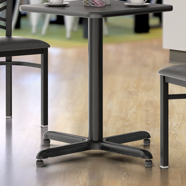 A black Lancaster Table & Seating standard height table base with a wood table top and chairs.