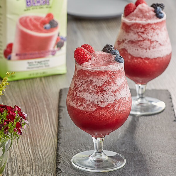 Two glasses of red fruit smoothie with berries on top.