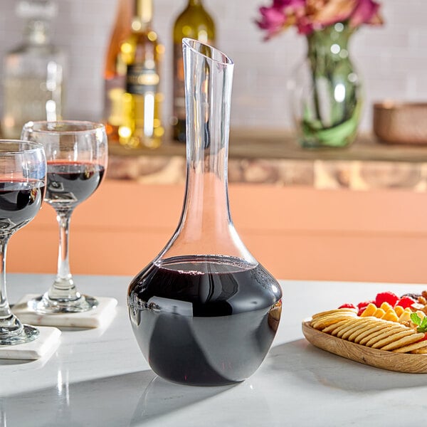 A Franmara Fleurie crystal decanter filled with red wine on a table with a plate of fruit and crackers.