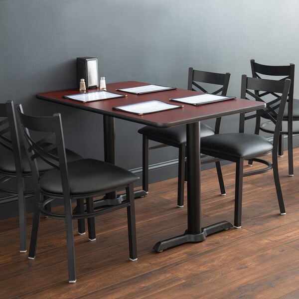 Wood table with four menus on top and four black chairs in restaurant
