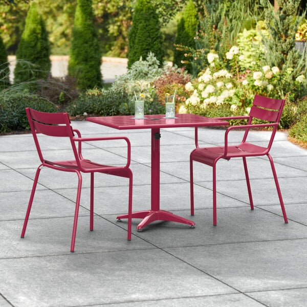 A red powder-coated aluminum Lancaster Table & Seating outdoor table with two chairs on a concrete patio.