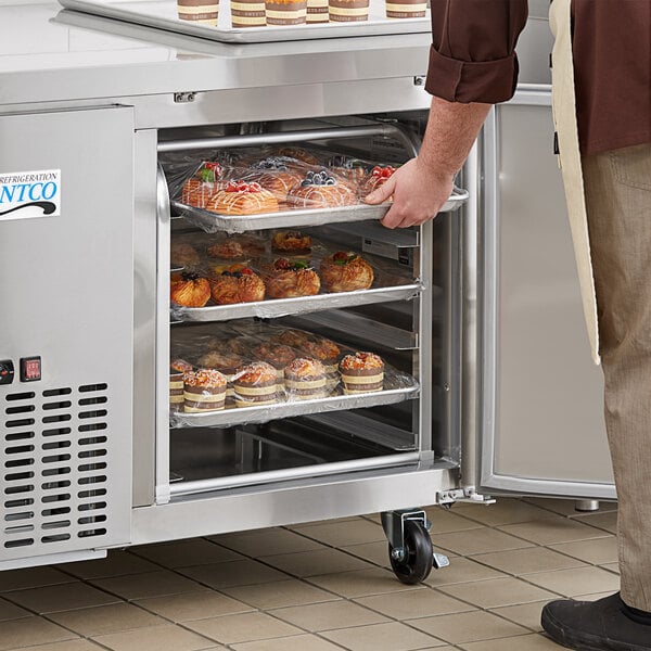 A man standing in front of an unassembled Regency 6 pan sheet pan rack taking food out of a refrigerator.