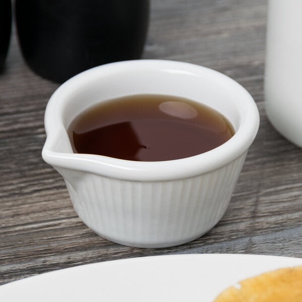 A close up of a white Tuxton fluted ramekin with brown liquid in it.