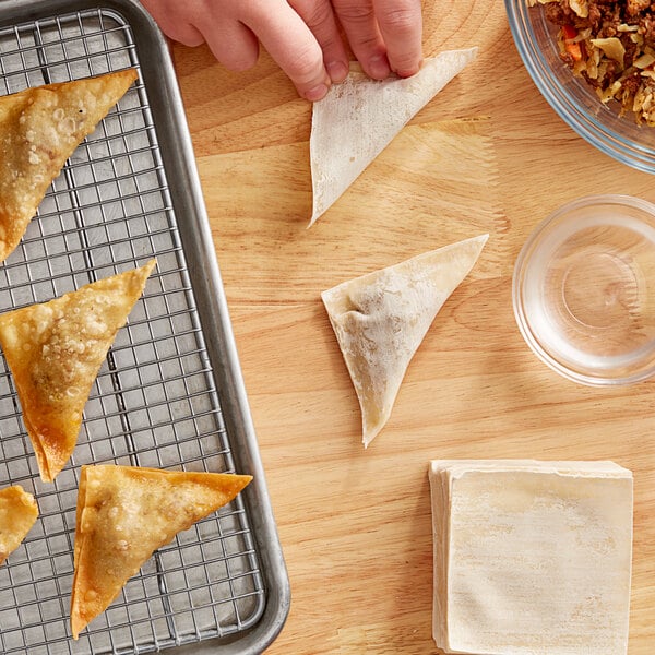 A person placing fried Golden Tiger Wonton Wrapper triangles onto a metal rack.