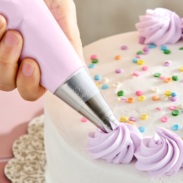 An open star piping tip being used to decorate a cake with purple icing swirls.