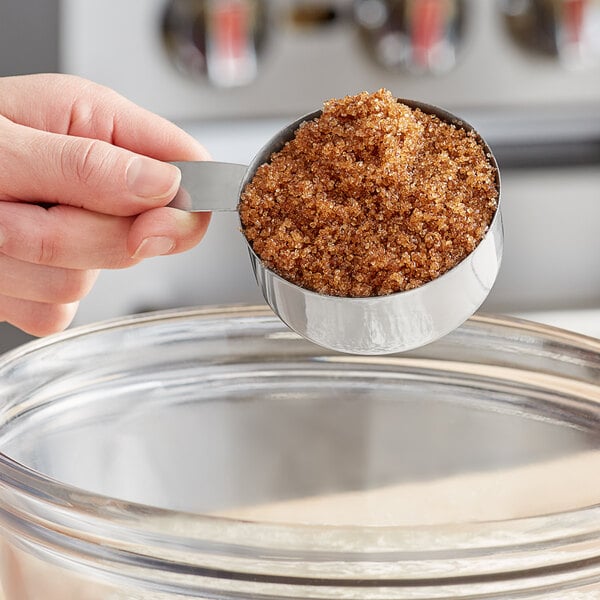 A person holding a measuring cup with Florida Crystals Organic Dark Brown Cane Sugar.
