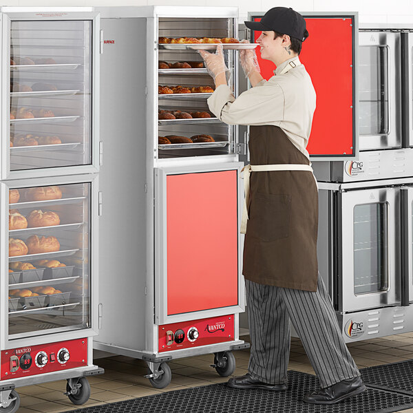 A man wearing a brown apron standing in front of an Avantco heated holding cabinet with solid Dutch doors.