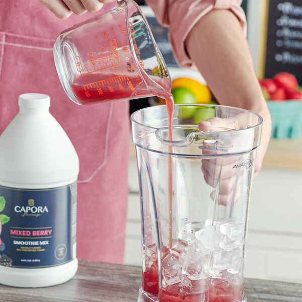 A hand pouring Capora mixed berry smoothie mix into a blender.