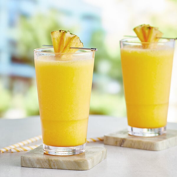 A couple of glasses of yellow liquid with pineapple slices on a table.