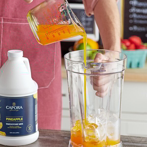 A hand pouring Capora Pineapple Fruit Smoothie Mix into a blender.