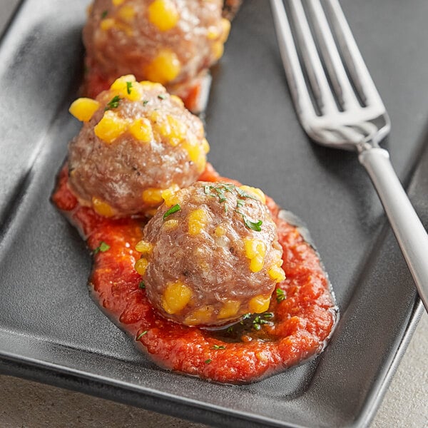 A black plate of meatballs with yellow cheese sauce on it with a fork.