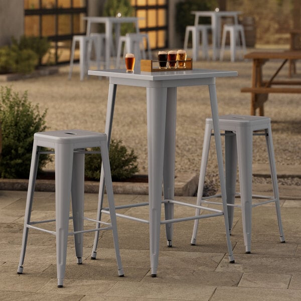 A Lancaster Table & Seating nickel gray outdoor bar height table with two backless barstools on a patio.
