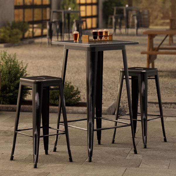 A Lancaster Table & Seating black metal bar table with two black metal barstools.