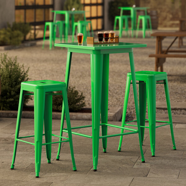 A Lancaster Table & Seating jade green bar table with backless bar stools on a concrete outdoor patio.