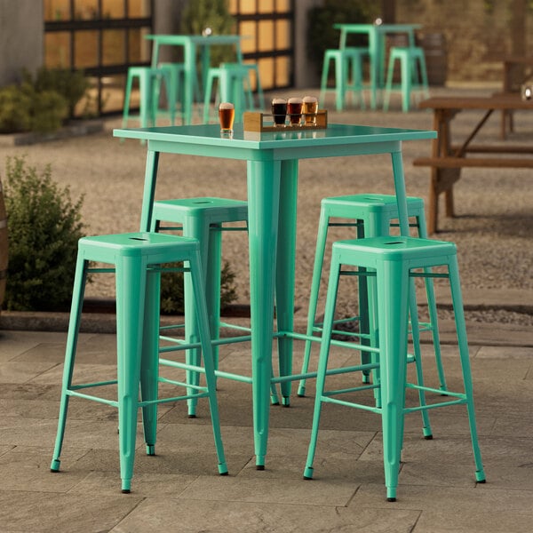 A Lancaster Table & Seating bar height outdoor table with a green finish and four green barstools on a stone patio.