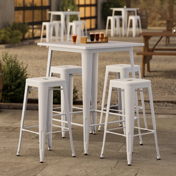 A Lancaster Table & Seating pearl white bar height table with four barstools outside on a patio.