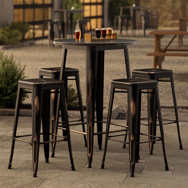 A Lancaster Table & Seating outdoor bar height table in distressed copper with four black backless barstools.
