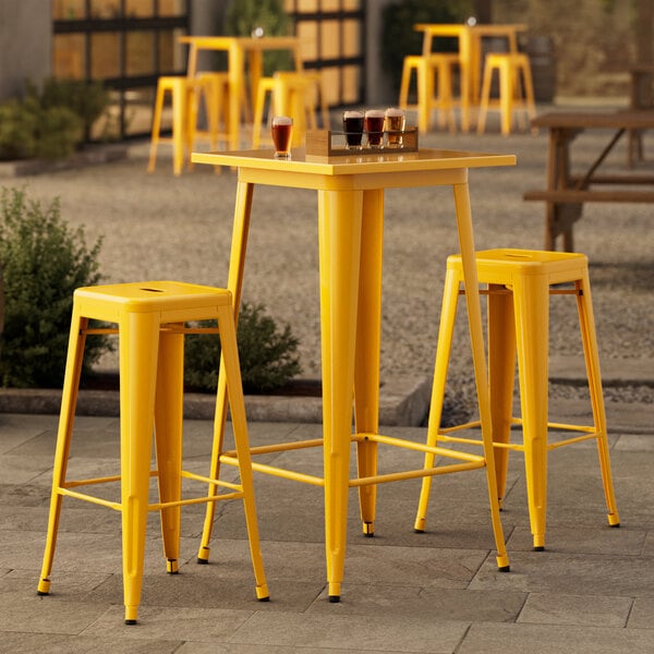 A Lancaster Table & Seating citrine yellow metal outdoor bar table with two yellow metal barstools.