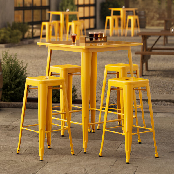 A Lancaster Table & Seating citrine yellow bar table with four stools on a patio.