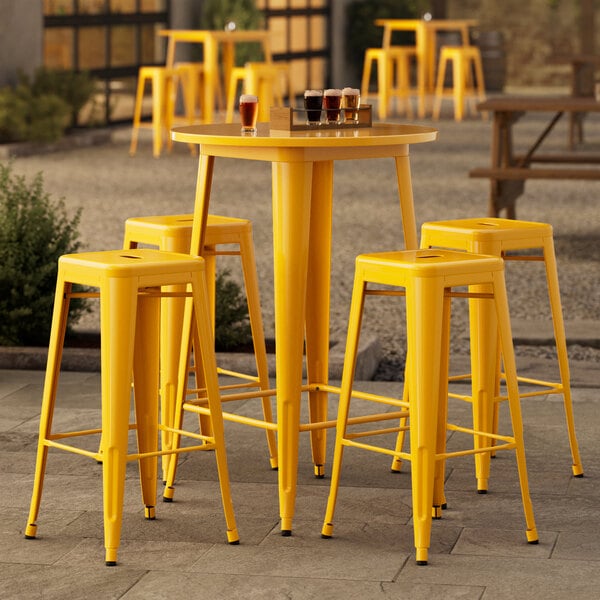 A Lancaster Table & Seating yellow bar height table with yellow stools on an outdoor patio.