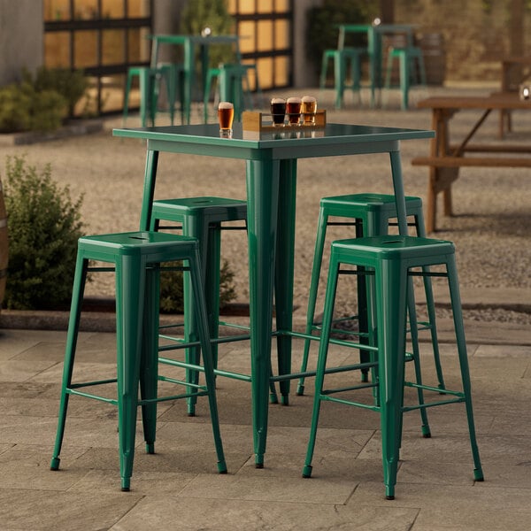 A Lancaster Table & Seating emerald green metal bar table with four backless bar stools on a stone patio.