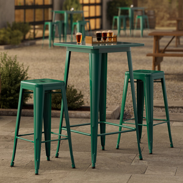 An emerald green metal bar table with two bar stools on an outdoor patio.