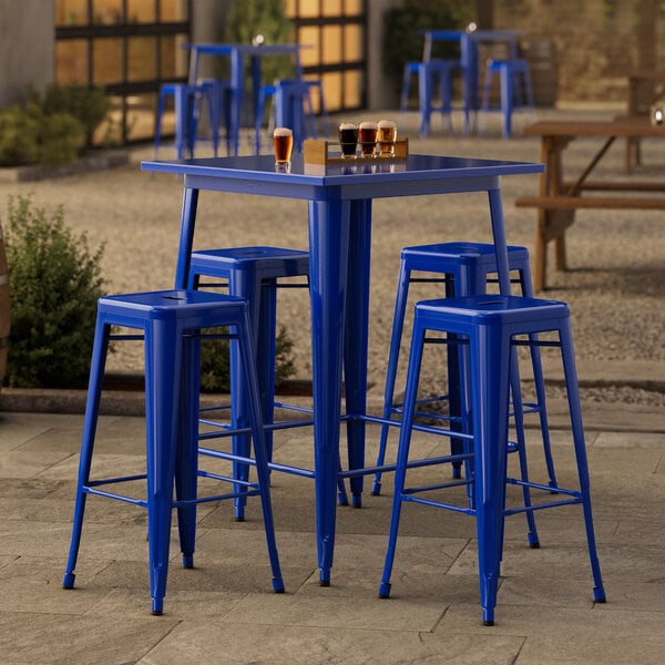 A blue square Lancaster Table & Seating bar table with four blue backless barstools.