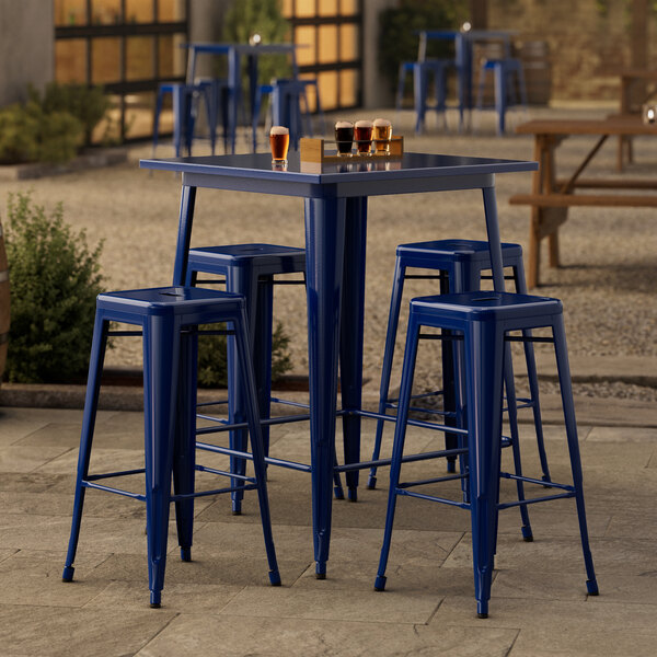 A square blue metal bar table with four blue stools on a stone patio.