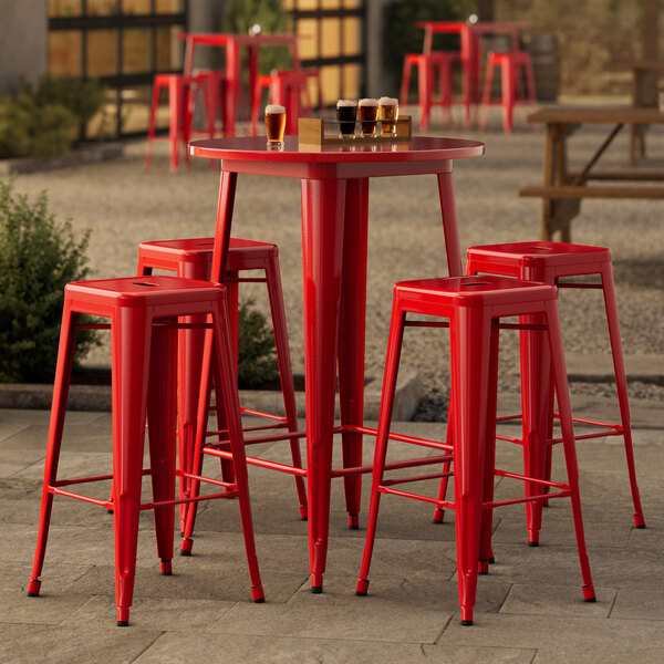 A Lancaster Table & Seating red metal bar table with four backless barstools on an outdoor patio.