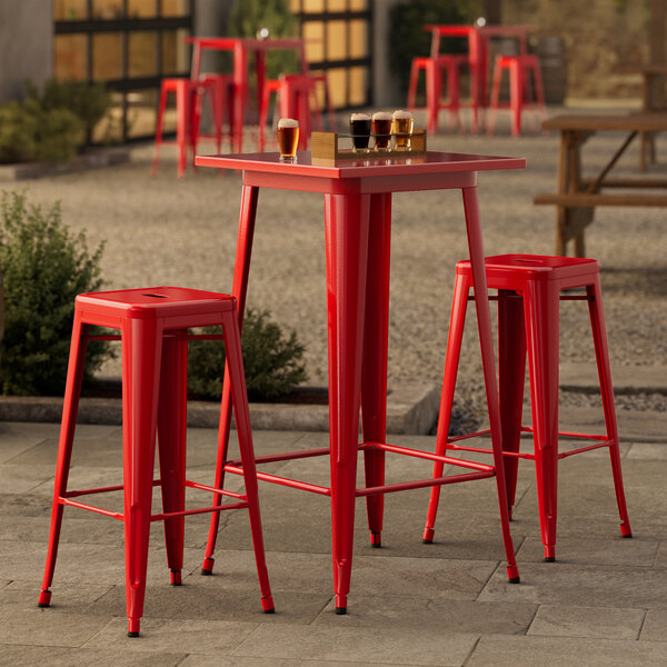 A Lancaster Table & Seating ruby red metal bar table with two backless barstools outside.