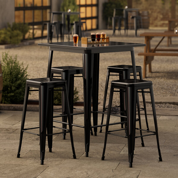 A Lancaster Table & Seating onyx black bar height outdoor table with four backless barstools on a patio.