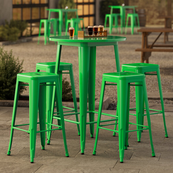 A Lancaster Table & Seating jade green bar height table with 4 green barstools outside on a stone patio.