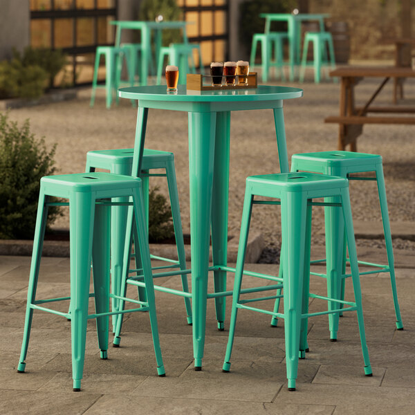 A Lancaster Table & Seating round aquamarine outdoor table with four green stools.