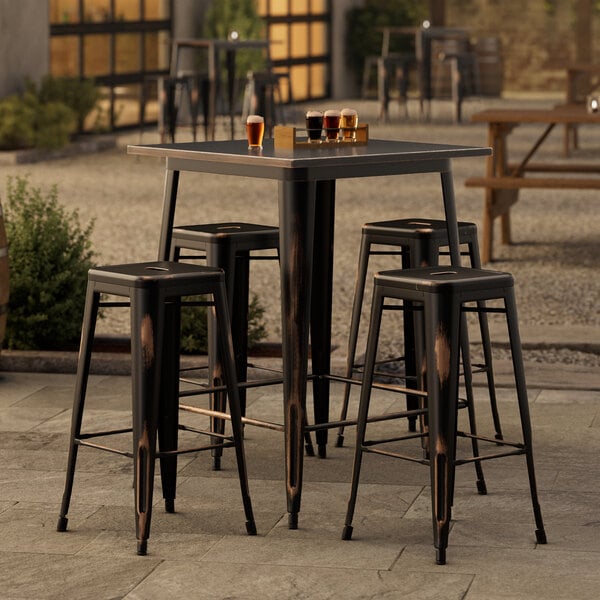 A Lancaster Table & Seating distressed copper bar height outdoor table with stools and glasses on top.