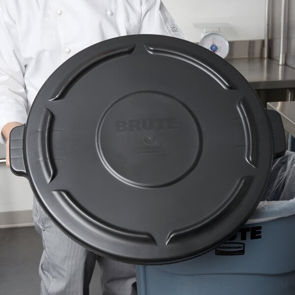 A person placing a Rubbermaid BRUTE black lid on a black trash can.