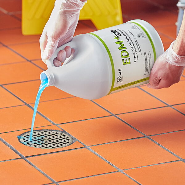 A hand in a plastic glove pouring Noble Eco EDM+ Ultra liquid into a drain.