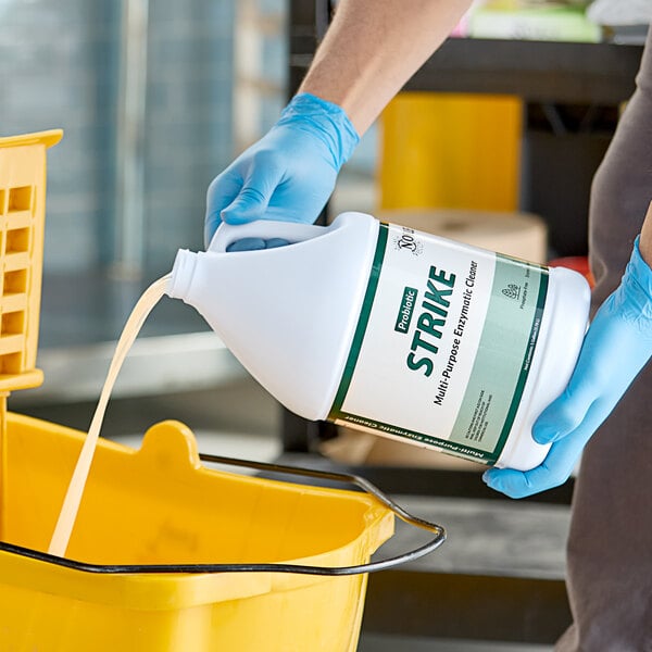A person in blue gloves pouring Noble Eco Strike multi-purpose enzymatic cleaner into a bucket.