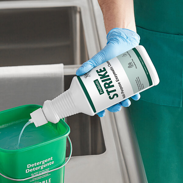 A person in blue gloves pouring Noble Eco Strike multi-purpose enzymatic cleaner into a container.