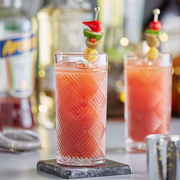 Two Acopa highball glasses filled with red cocktails with garnish on a table.