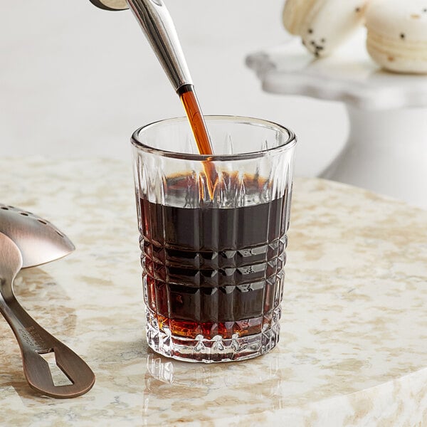 A Acopa Madras shot glass with a brown liquid being poured into it.