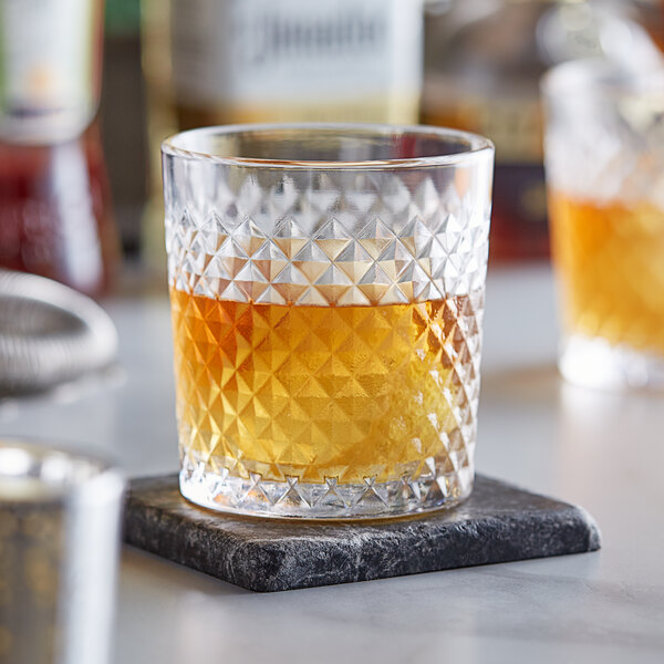 An Acopa Aurelius rocks glass of amber liquid on a stone coaster.