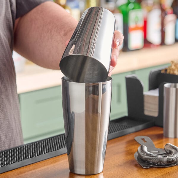 A bartender pouring a drink into a Barfly stainless steel cocktail shaker.