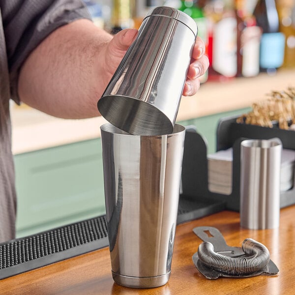 A bartender pouring a drink into a Barfly stainless steel cocktail shaker.