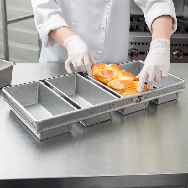 A person in a white coat holding a loaf of bread in a Chicago Metallic aluminized steel bread loaf pan.